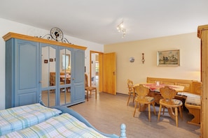Et værelse med en seng, et træspisebord med stole, en blå garderobe og en dør til et andet rum.