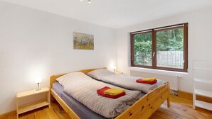 A room with a wooden bed, a bedside table, a window with a view of greenery, and a painting on the wall. - Bungalow 'Urlaubsoase Am Bruchsee' with Lake View, Private Terrace and Private Garden (Templin)