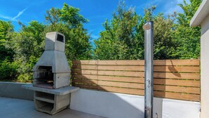 An outdoor barbecue area with a concrete grill, wooden fence, and a metal pole. - Holiday home Ella (Privlaka)