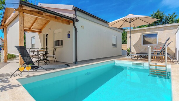 A swimming pool with lounge chairs and umbrellas, a covered patio area, and a stone wall. - Holiday home Ella (Privlaka)