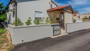 A modern two-story house with a grey exterior, a red-tiled roof, and a small porch with a table and chairs. - Holiday home Ella (Privlaka)