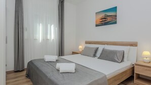 A modern bedroom with a large bed, grey bedding, wooden headboard, bedside lamps, and a painting on the wall. - Holiday home Ella (Privlaka)