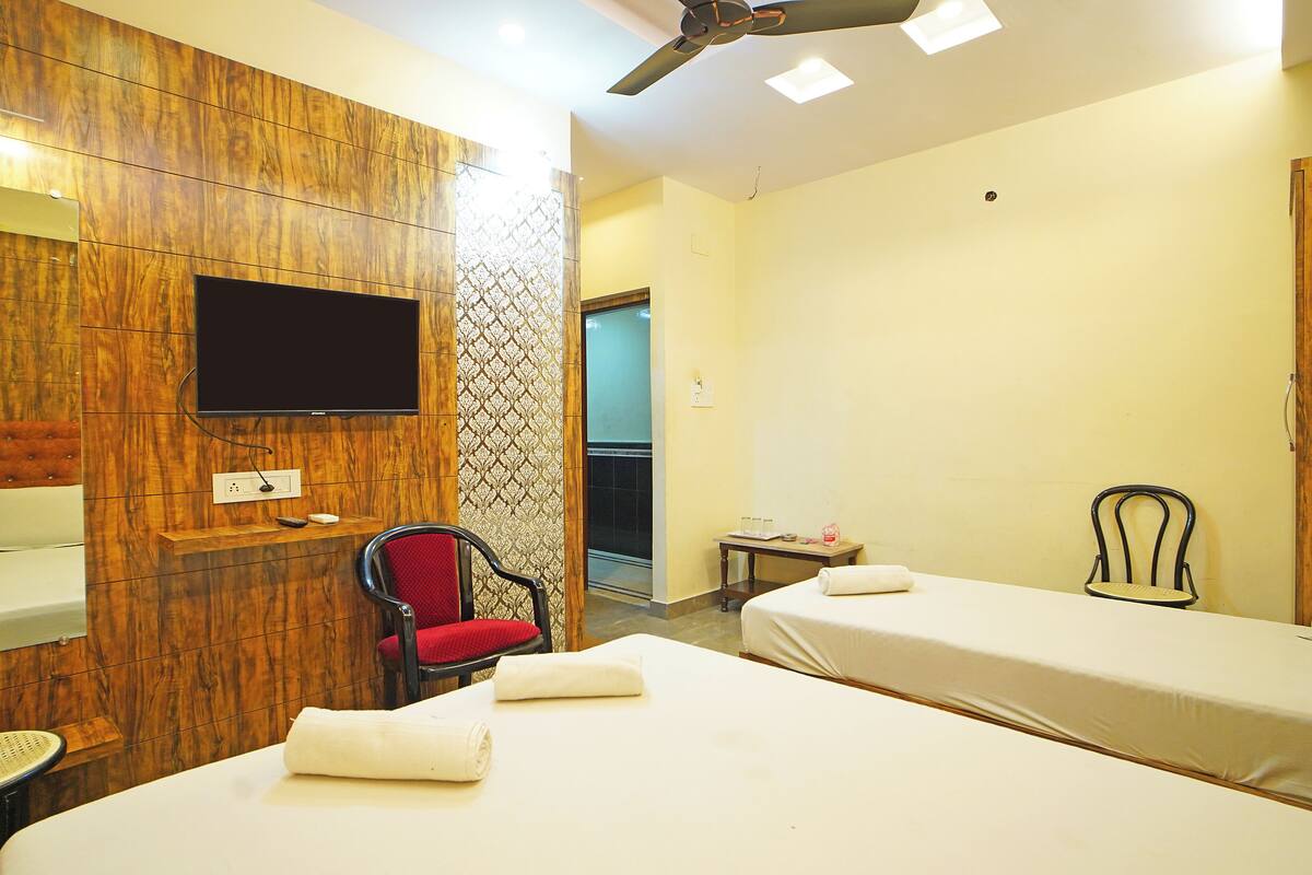 A hotel room with two beds, a TV mounted on the wall, a red chair, and a small table with a chair.