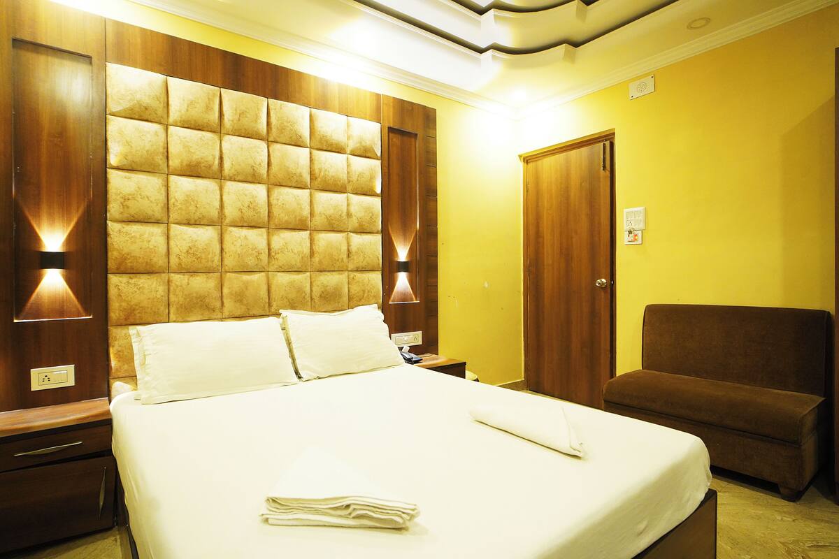 A hotel room with a large bed, wooden headboard, two bedside tables, a brown armchair, and a wooden wardrobe.
