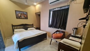 A bedroom with a bed, a chair, a table with a kettle, and a wall-mounted air conditioner.