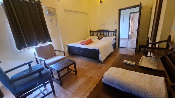 A hotel room with a bed, a chair, a small table, and a wooden floor.