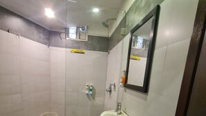 A small, tiled bathroom with a sink, a mirror, and a shower stall.