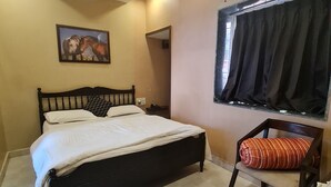 A bedroom with a bed, a chair, an air conditioning unit, a window with curtains, and a wall-mounted picture.