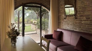 Une pièce dotée d’un coin salon avec des sièges confortables, d’une table ornée d’un vase de fleurs et offrant une vue sur un jardin grâce à une porte vitrée.
