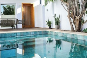 A modern outdoor pool area with a wooden door, a dining set, and potted plants. - Escape Newspaper: Sumptuous villa with swimming pool  (La Marsa)