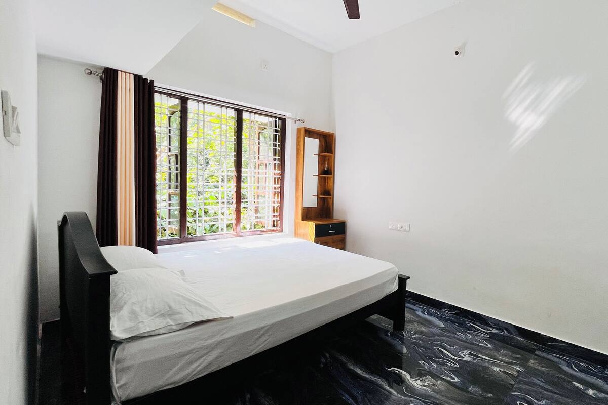 A small, single-bed room with a window, a wooden nightstand, and a built-in shelf.