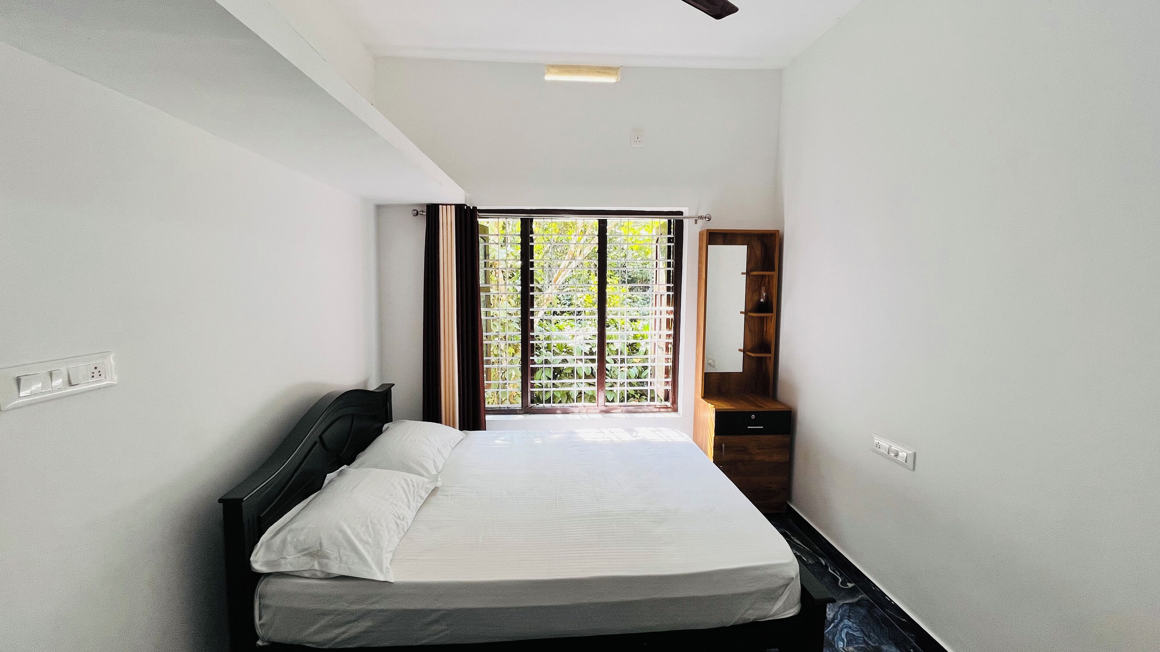 Un dormitorio con cama, mesita de noche, espejo y ventana con vistas a zonas verdes.