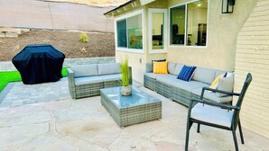 An outdoor patio with wicker furniture, a glass-top coffee table, and a grill.