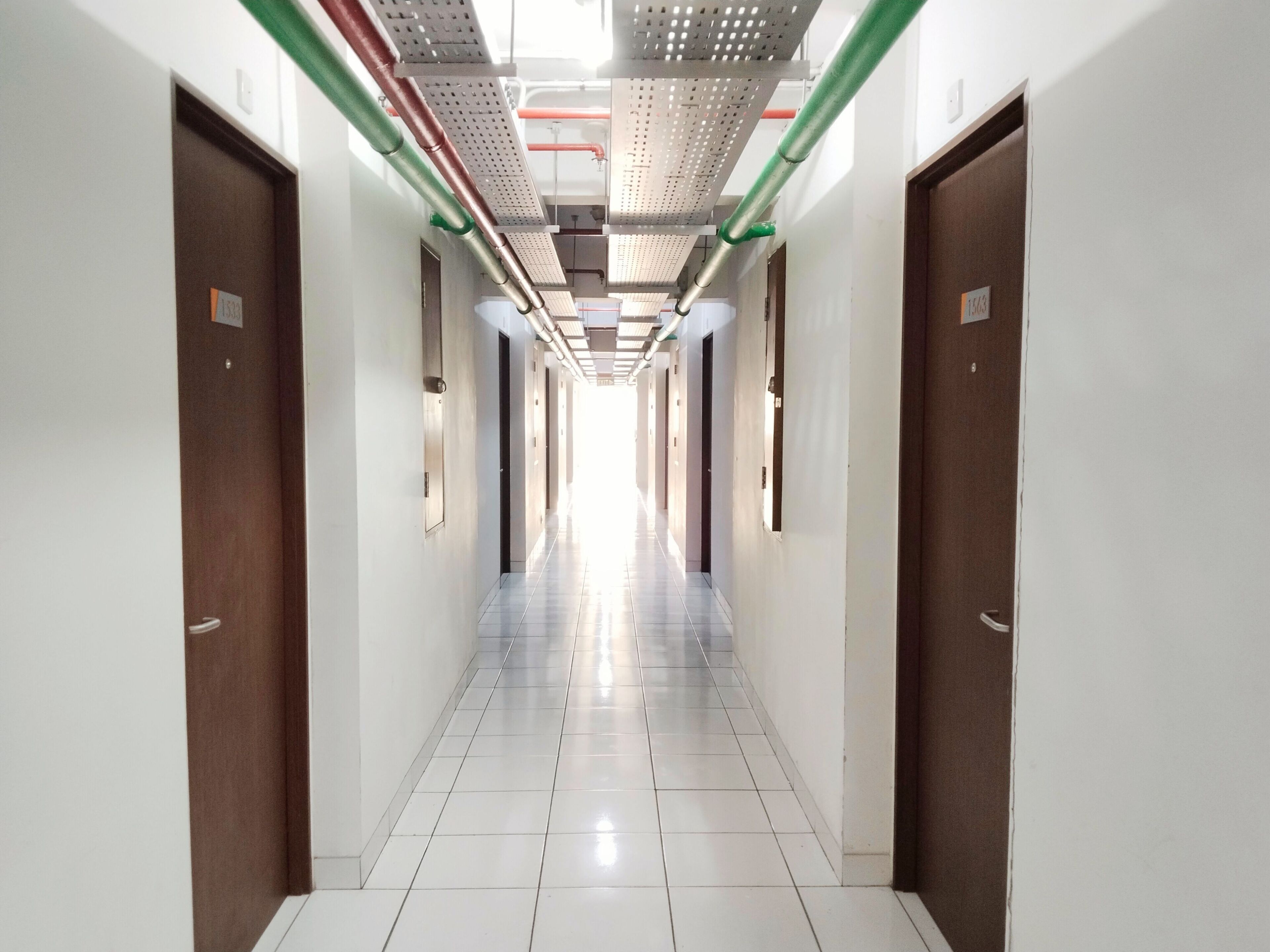 A long, narrow hallway with white tiled floors and doors on both sides.