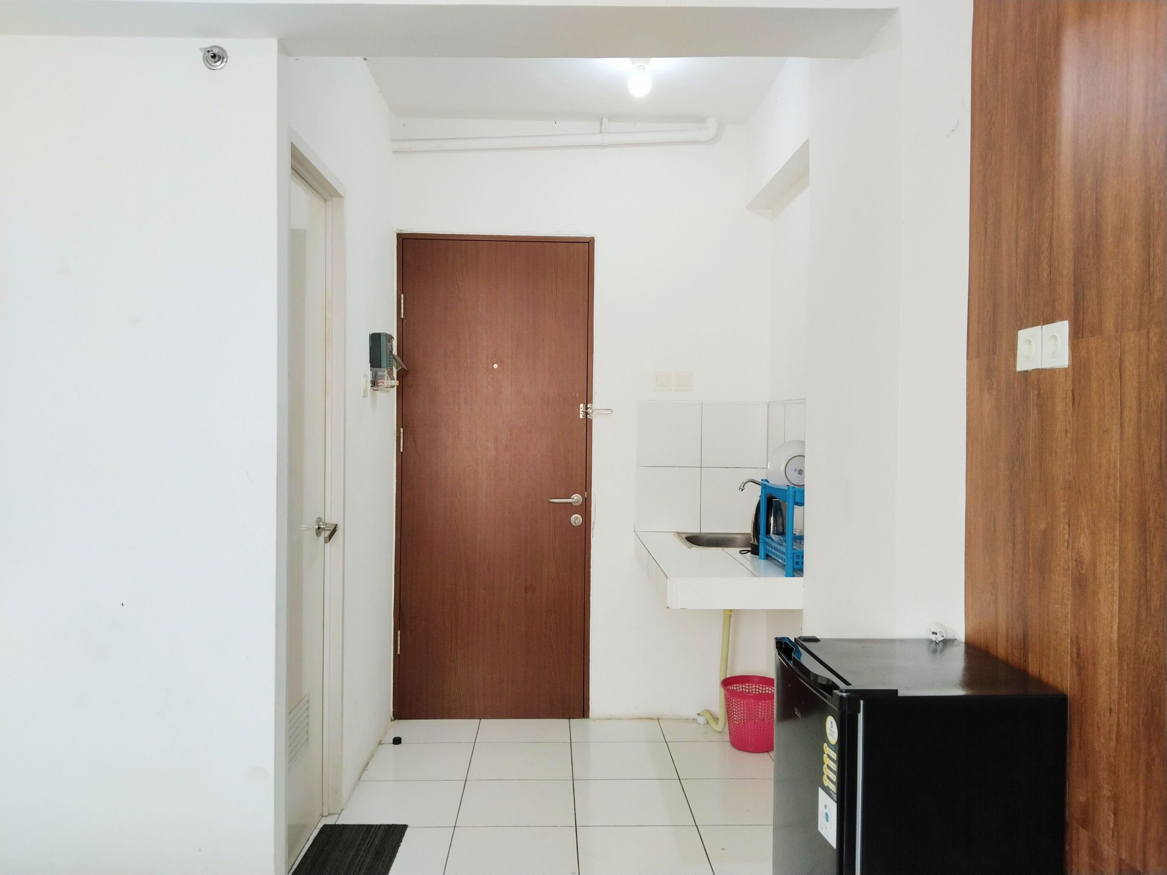 A small, clean room with a wooden door, a white sink, and a black refrigerator.