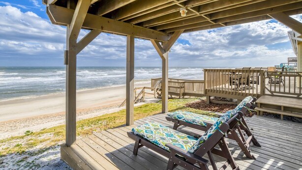 Eine Holzterrasse am Strand mit Liegestühlen und Blick auf das Meer.