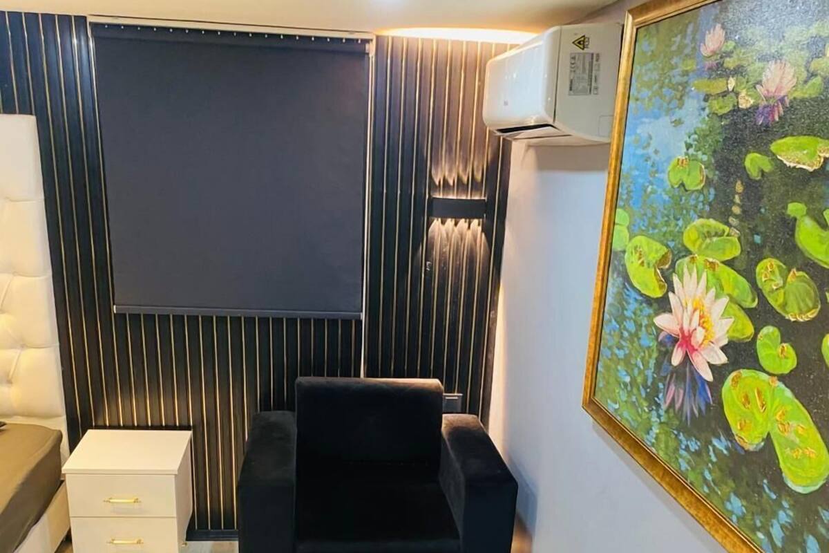 A room with a black sofa, a small white bedside table, a black ottoman, and a large framed painting of water lilies.