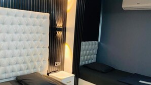 A modern bedroom with a tufted headboard, a bedside table, a bed with dark bedding, and an air conditioning unit. - Montenegro Suit Hotel (Eyup)