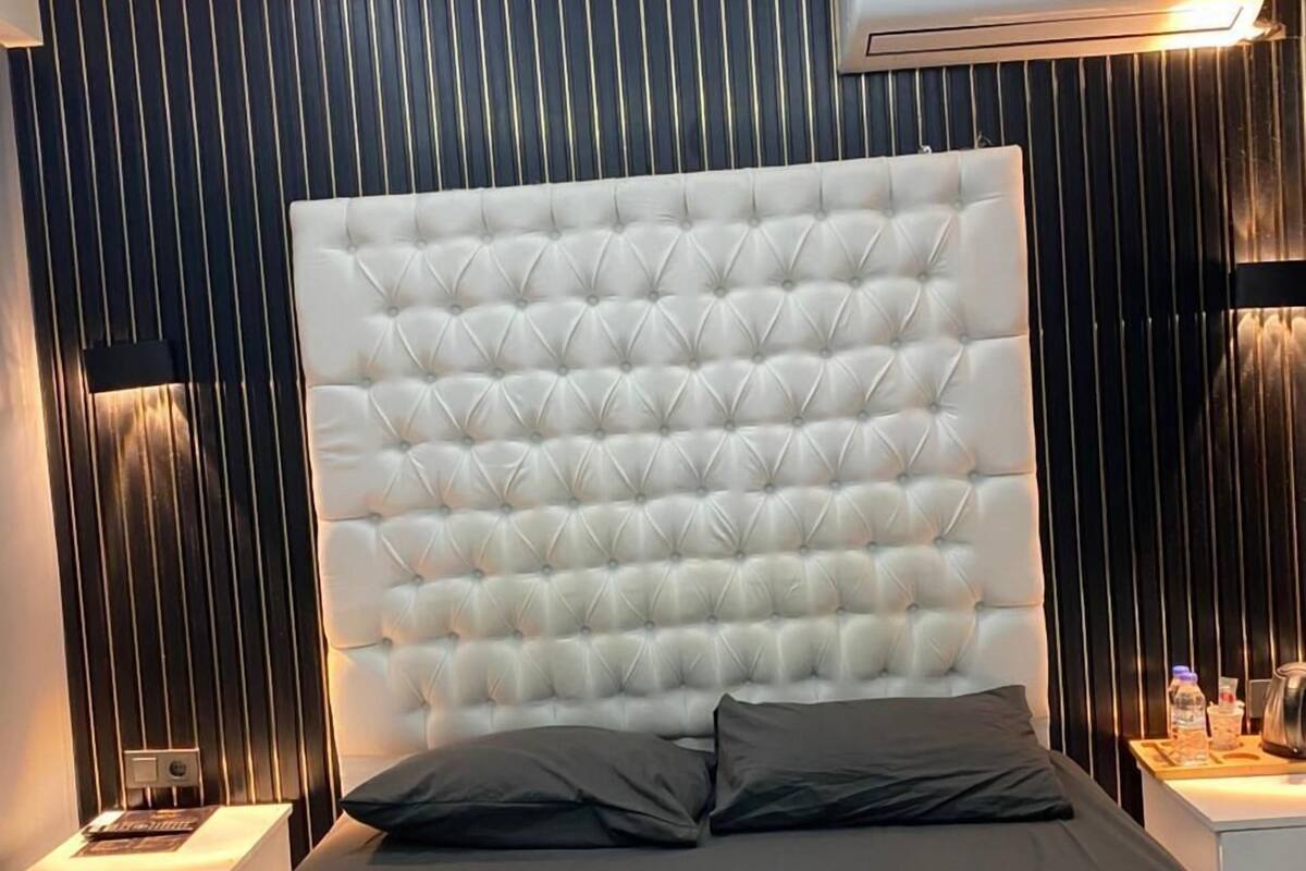 A modern bedroom with a tufted headboard, a skylight, and a bedside table with a lamp.