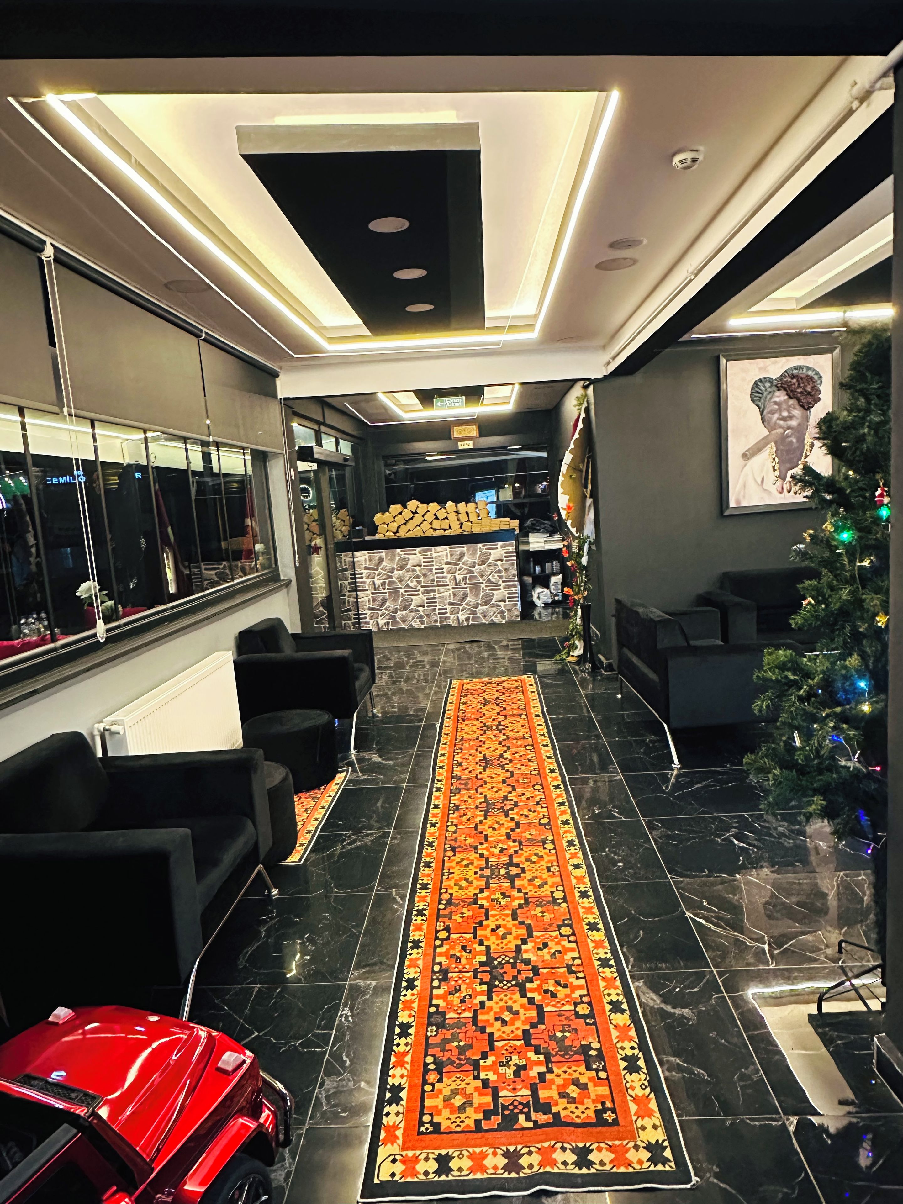 A hotel lobby with a black marble floor, a red sports car, a Christmas tree, and a patterned rug.