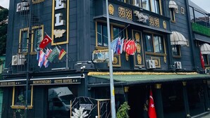 A black building with 'HOTEL' signage, multiple flags, and a balcony. - Montenegro Suit Hotel (Eyup)