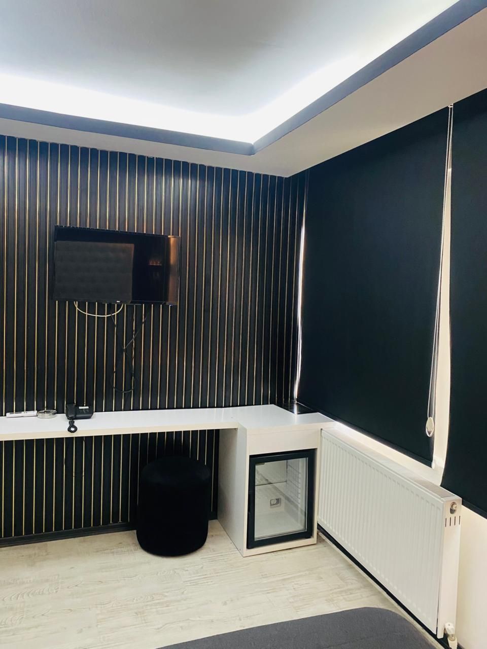 Una habitación moderna con techo inclinado, televisor montado, escritorio blanco, silla negra y radiador.