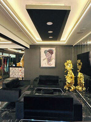 Un interior moderno con un sofá negro, una obra enmarcada y un reloj dorado.
