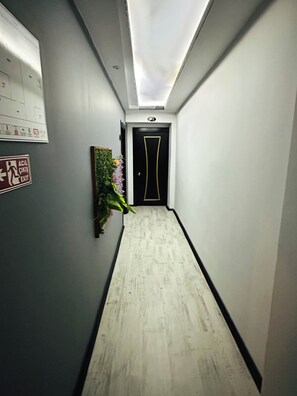 A narrow hallway with a door at the end, a wall-mounted emergency exit sign, and a potted plant.