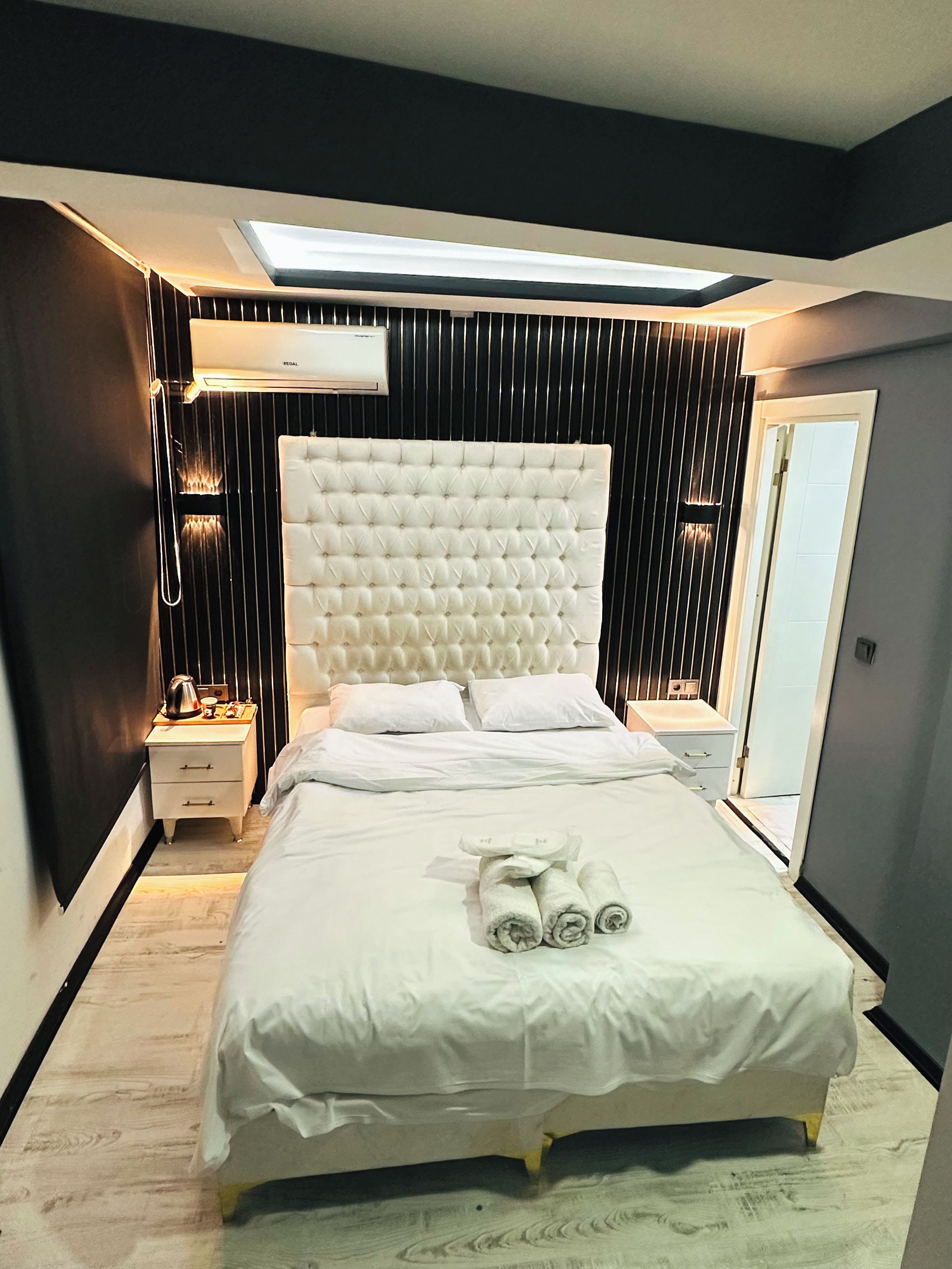 A modern bedroom with a tufted headboard, a neatly made bed with white linens, and a set of towels on the bed.