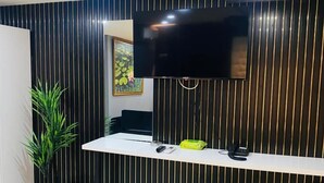 A modern reception area with a flat-screen TV, a white reception desk, a potted plant, a trash bin, and a telephone. - Montenegro Suit Hotel (Eyup)
