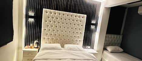 A modern hotel room with a large bed, a smaller bed, a bedside table, and a wall-mounted air conditioning unit.