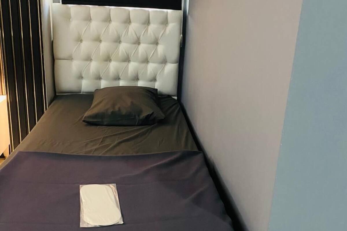 A small, single-bed room with a tufted headboard, a dark mattress, and a pillow.