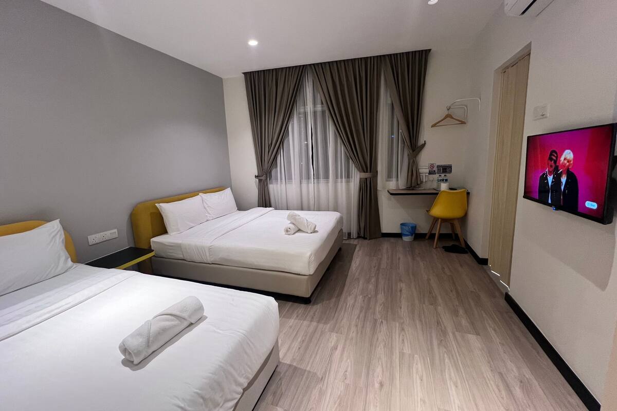 A hotel room with two beds, a desk, a TV, and a window with curtains.