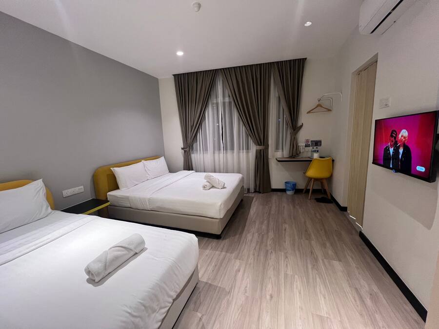 Habitación de hotel con dos camas, un escritorio, un televisor y una ventana con cortinas.