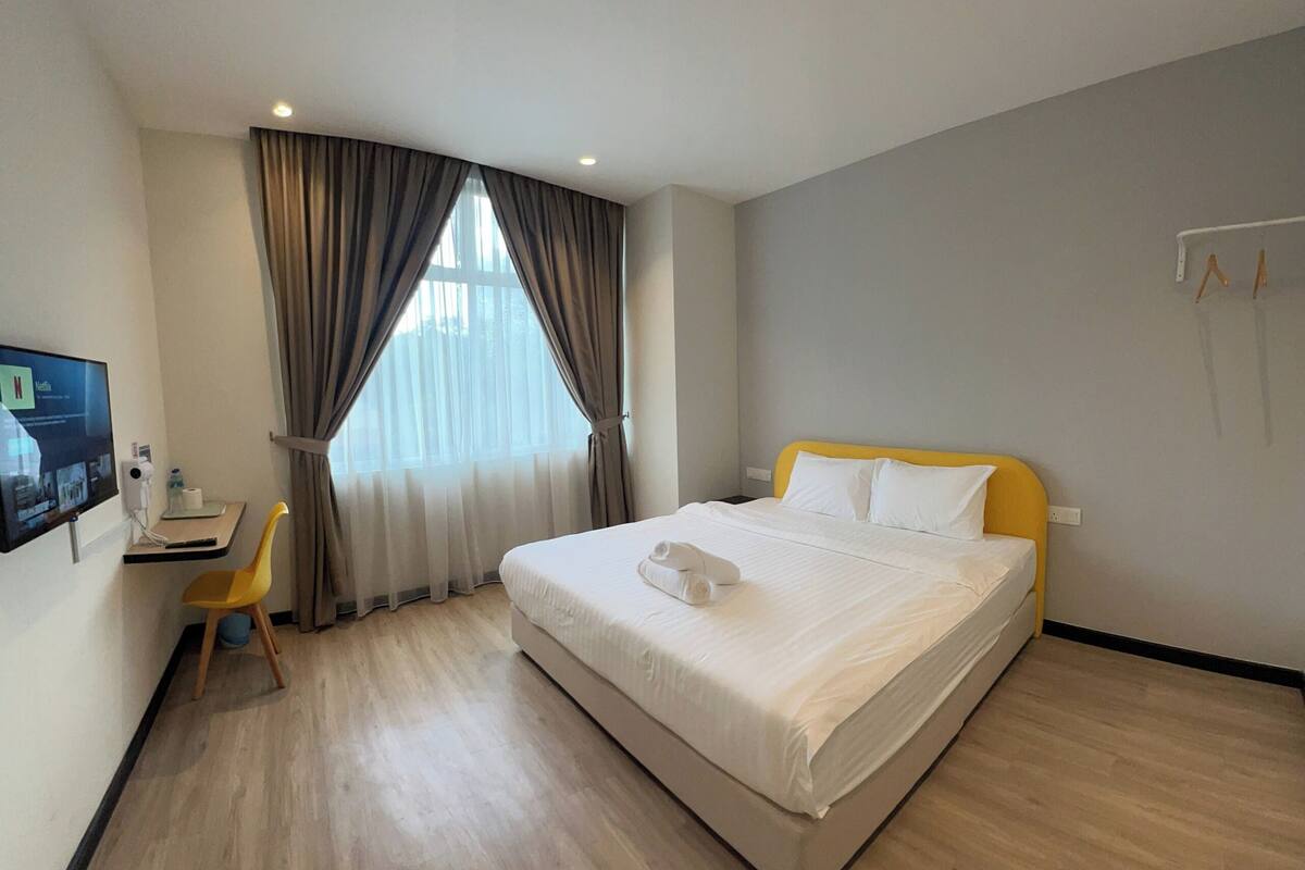 A hotel room with a bed, a desk, a chair, and a TV.