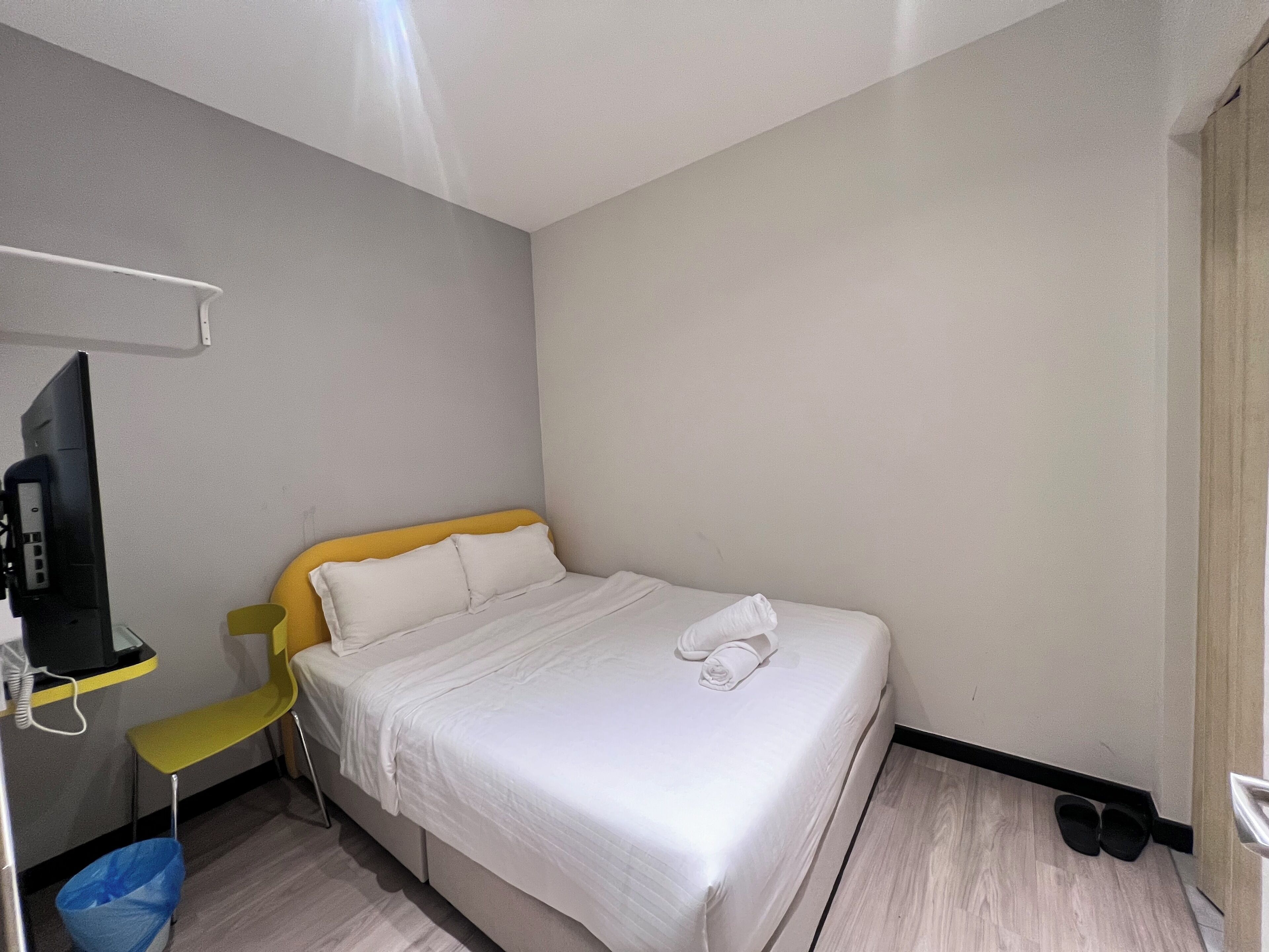 A hotel room with a single bed, a chair, a desk with a computer, and a TV.