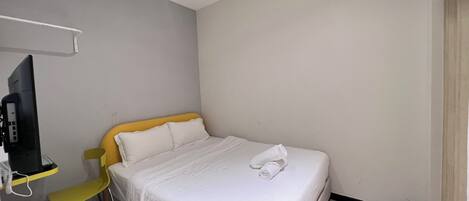 A hotel room with a single bed, a chair, a desk with a computer, and a TV.