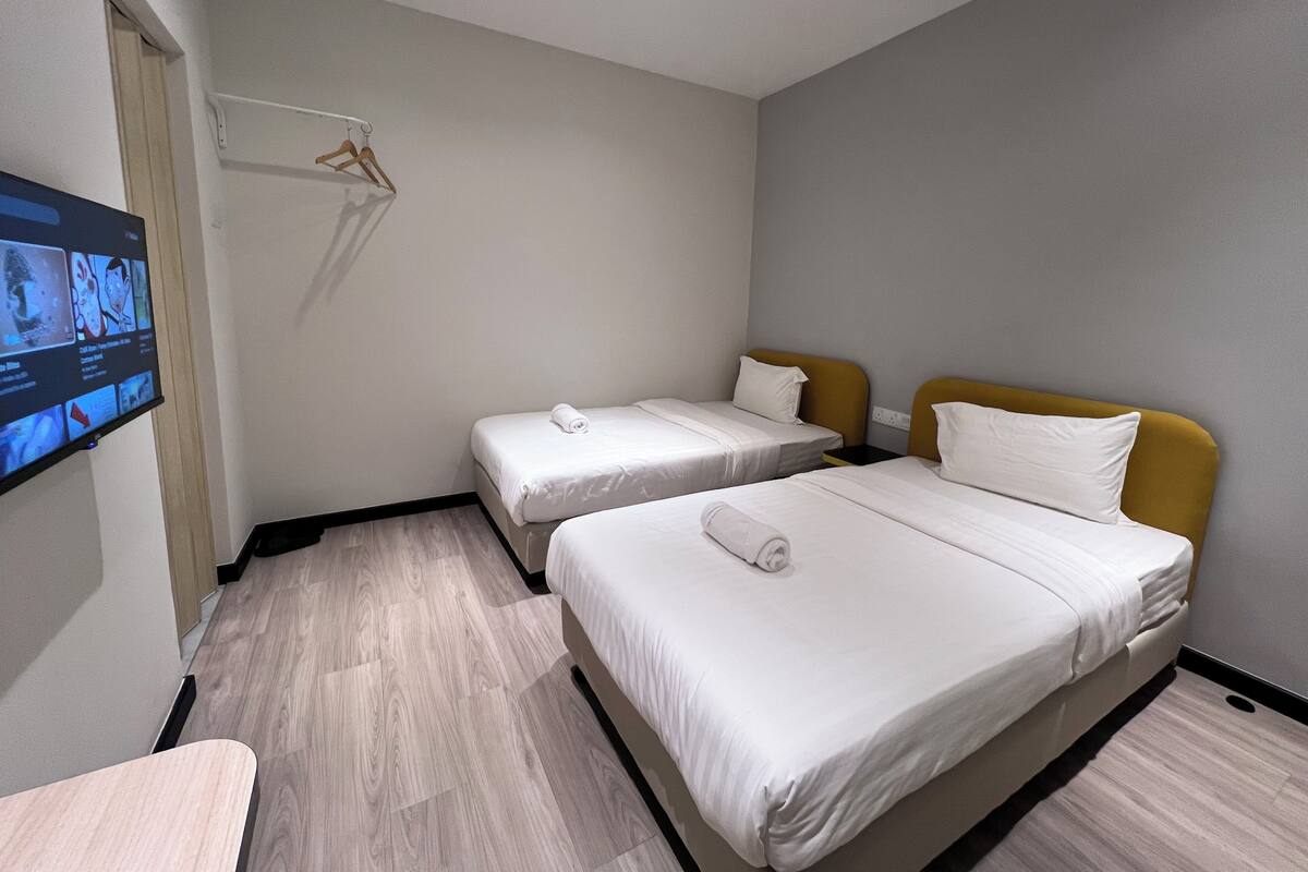A hotel room with two beds, a TV mounted on the wall, and a wooden floor.