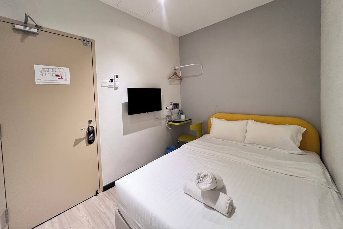 A hotel room with a bed, a TV mounted on the wall, a desk with a chair, and a door with a lock.