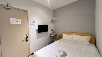 Habitación de hotel con cama, televisión montada en la pared, escritorio con silla y puerta con cerradura.