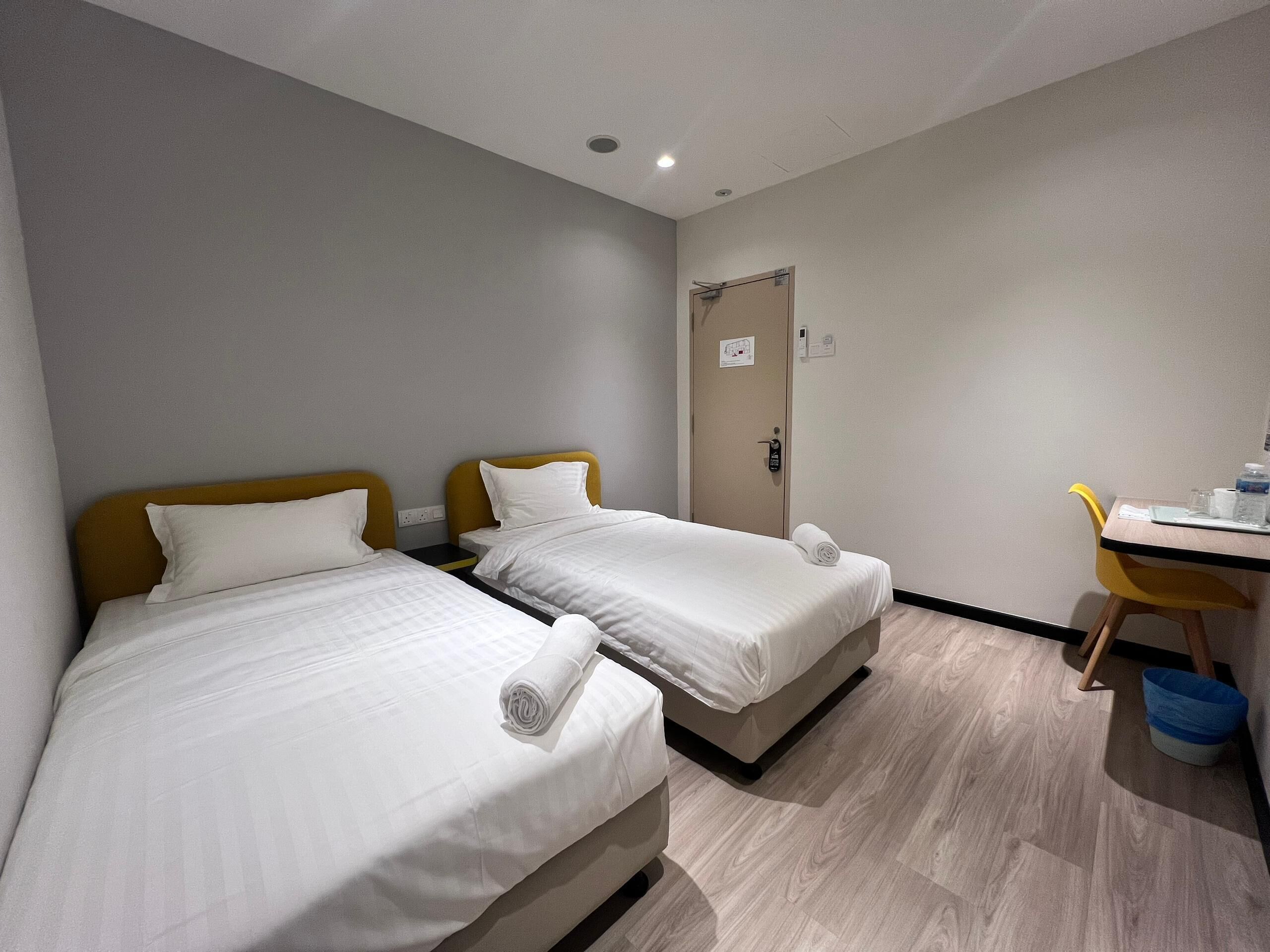 Quarto de hotel com duas camas, uma mesa e uma cadeira.