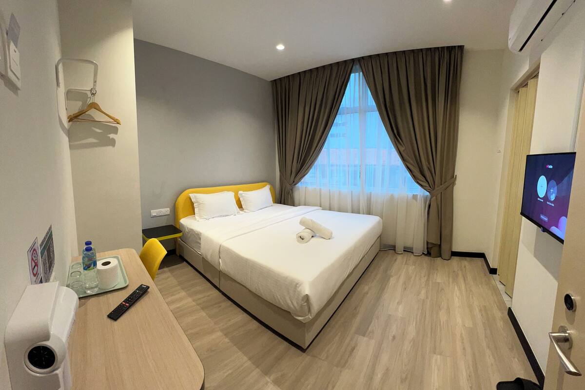 A hotel room with a bed, a desk, a TV, and a window with curtains.