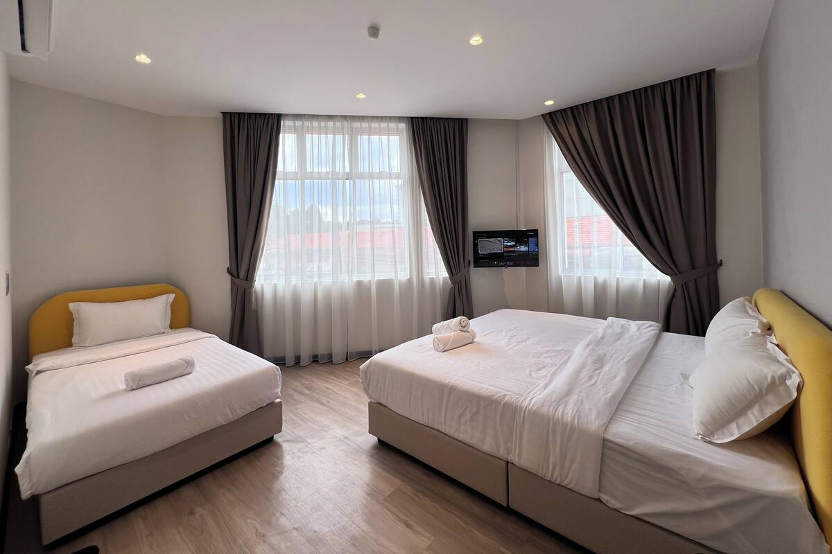 A hotel room with two beds, a flat-screen TV mounted on the wall, and a large window with curtains.