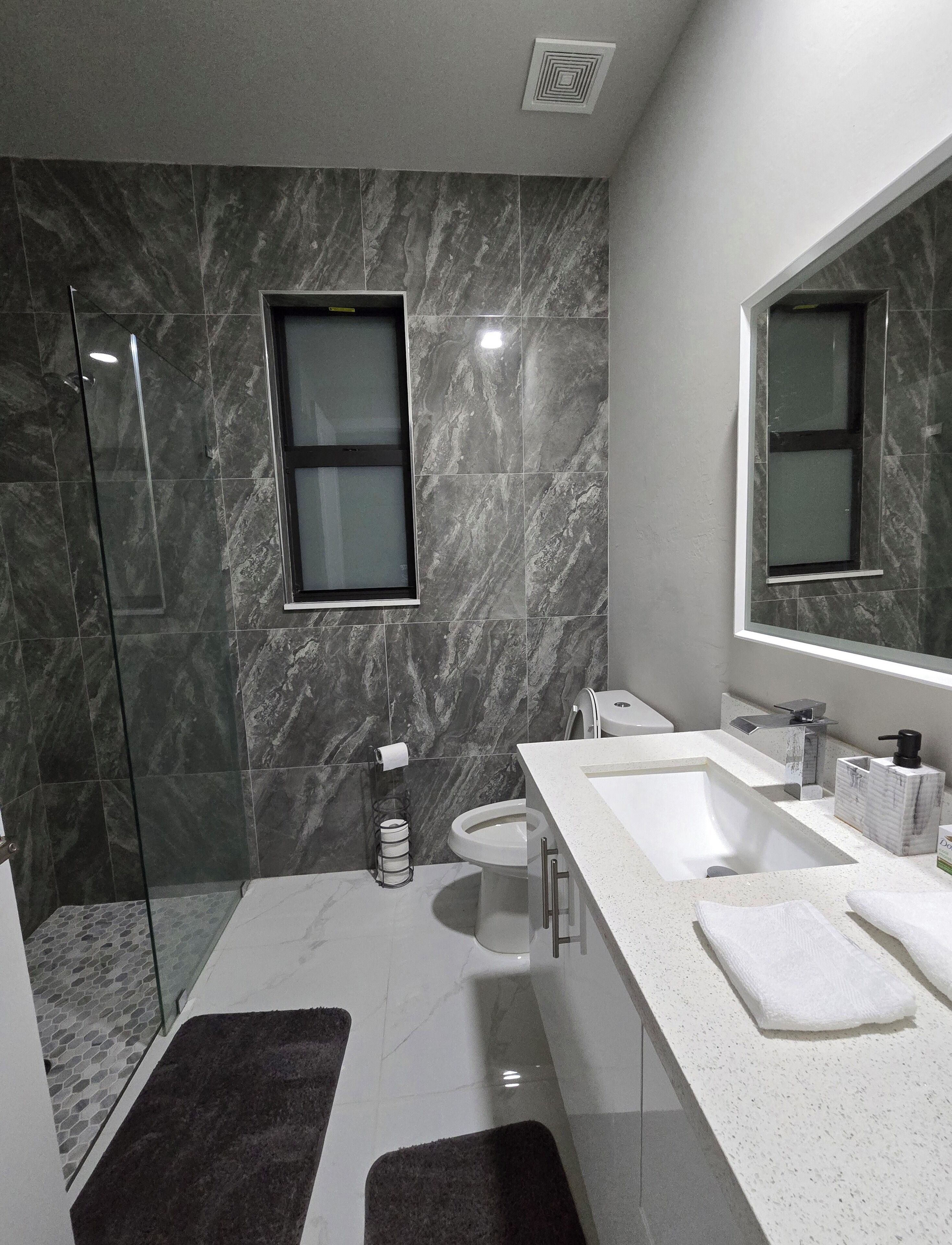 Une salle de bain moderne dotée d’une douche à parois de verre, de toilettes et d’un meuble-lavabo avec deux vasques et un grand miroir.
