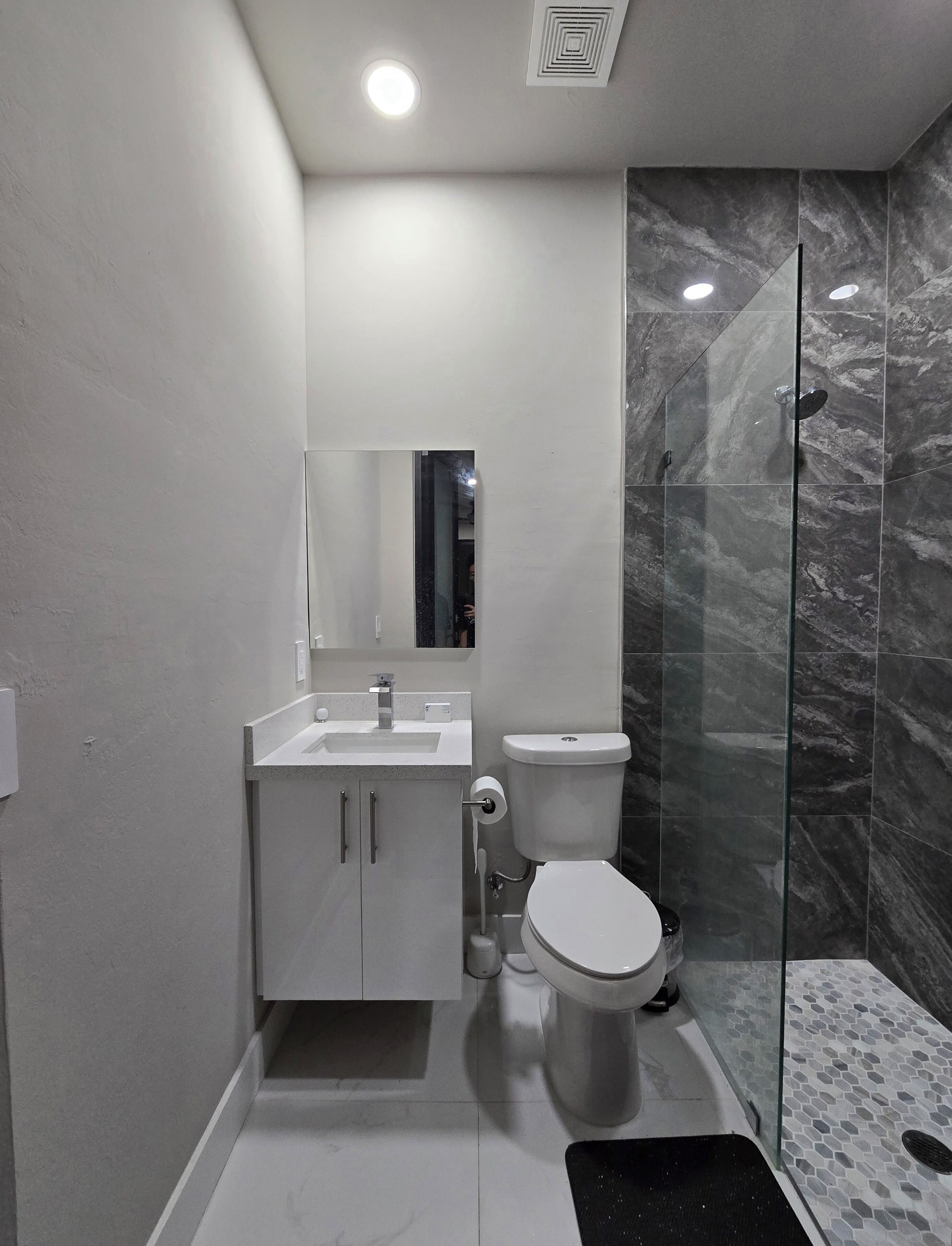 Une salle de bain moderne avec un lavabo blanc, un miroir et des toilettes, une douche en verre et des murs à motifs de marbre.