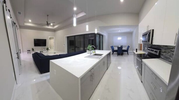 Una cocina moderna con una isla central, un comedor con mesa y sillas, y una sala de estar con sofá.