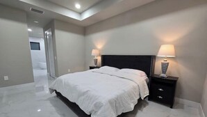 Un dormitorio moderno con una cama grande, dos mesitas de noche con lámparas y un baño al fondo.
