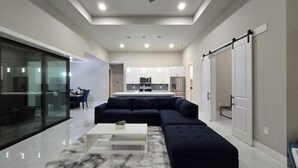 Una sala moderna con un sofá modular oscuro, una mesa de centro blanca y un separador de vidrio.