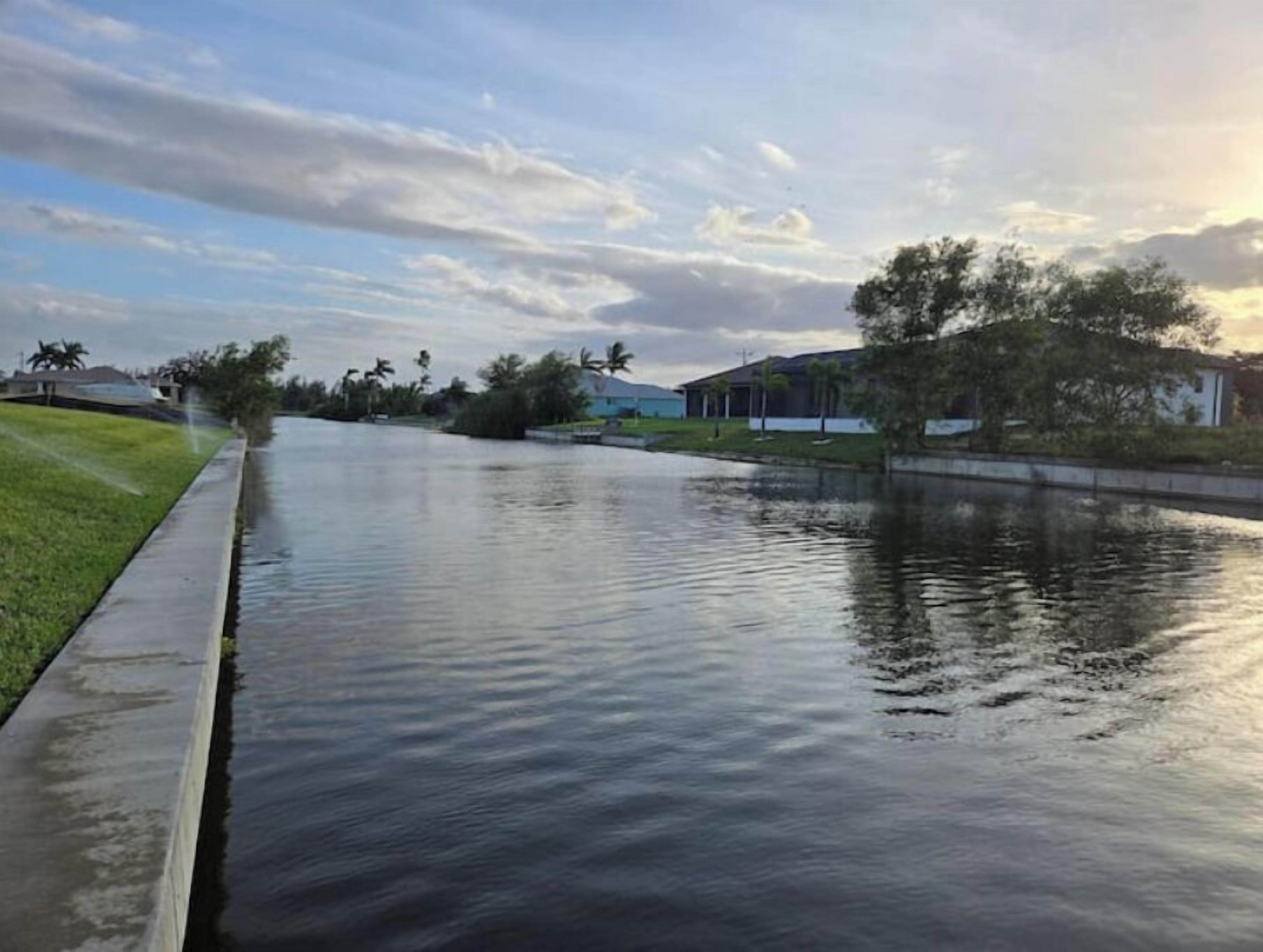 A calm waterway flanked by grassy areas and buildings, likely a canal or river in a residential area.