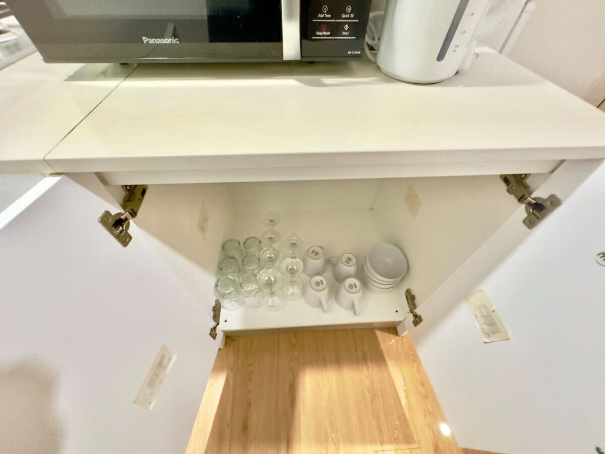 A kitchen with a microwave, a coffee maker, and a cabinet with glassware and bowls.